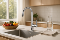A bright, modern kitchen styled like a premium lifestyle magazine. A sleek Grohe mixer tap is the centerpiece above a spotless sink, with sunlight streaming in from a nearby window. The countertop features fresh produce in a wooden bowl, a glass carafe filled with water, and a neatly folded linen towel. Clean lines, stainless steel details, and warm wooden accents create an atmosphere of modern elegance — showcasing the tap as the perfect blend of design and functionality.